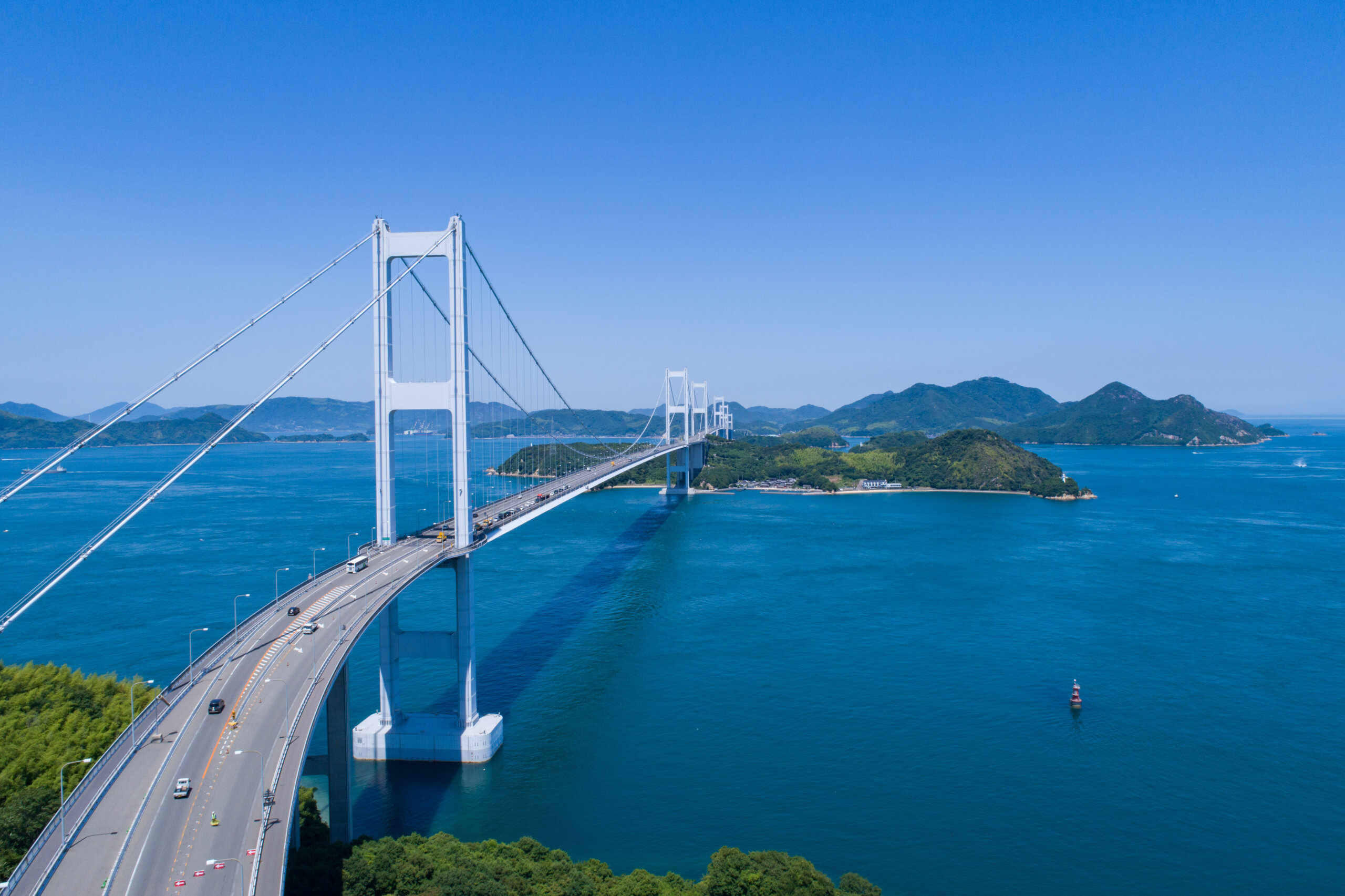 White suspension bridge crossing a blue sea with green islands and a clear sky.